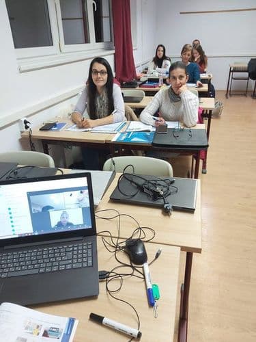 előtérben laptop, háttérben oktatók órán figyelnek